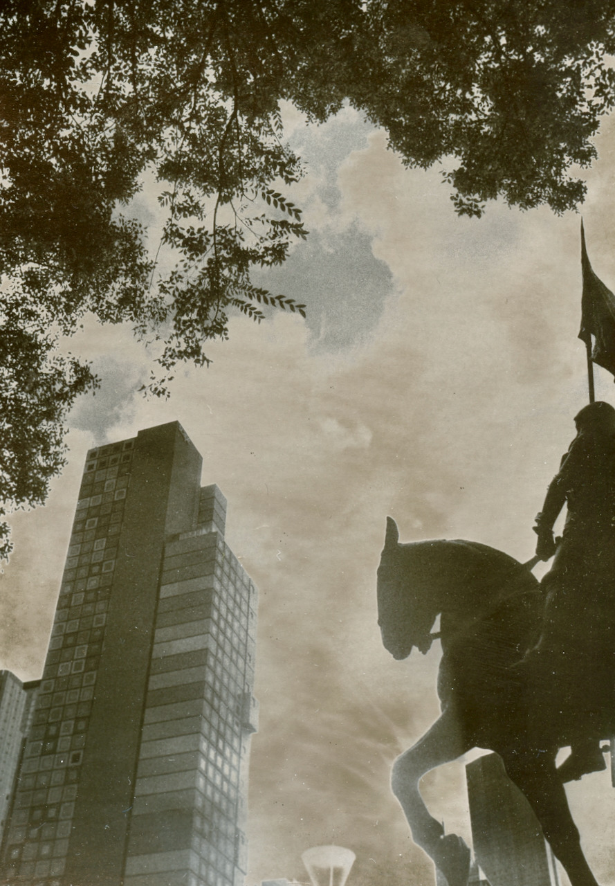 Equestrian statue and a modernist tower seen through overhanging foliage, printed with a warm silvered sky