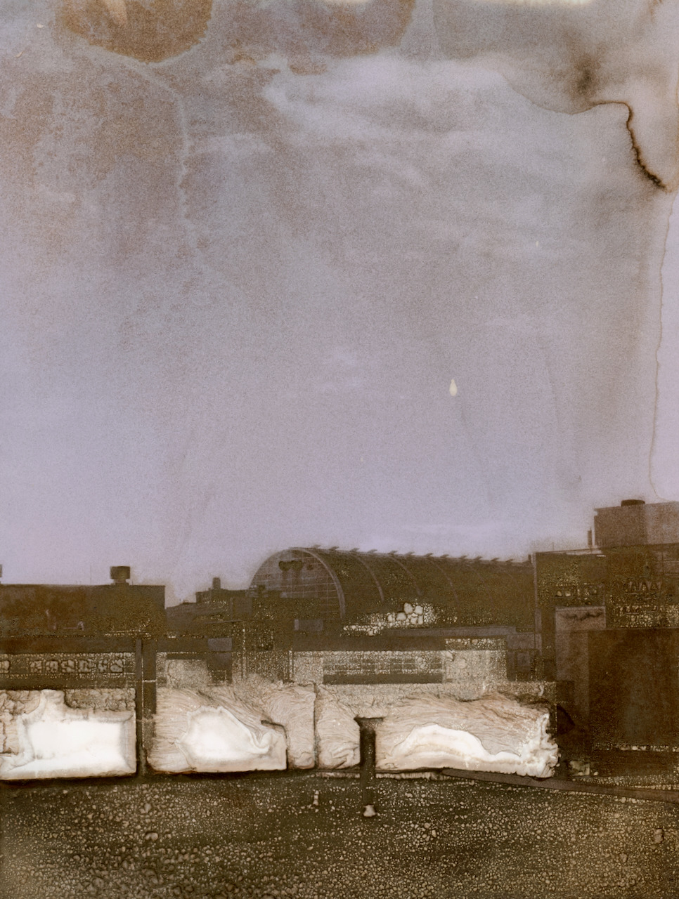 Industrial rooftops under a lilac sky, with gold-brown mordançaged shadows and bleached white forms along the roofline