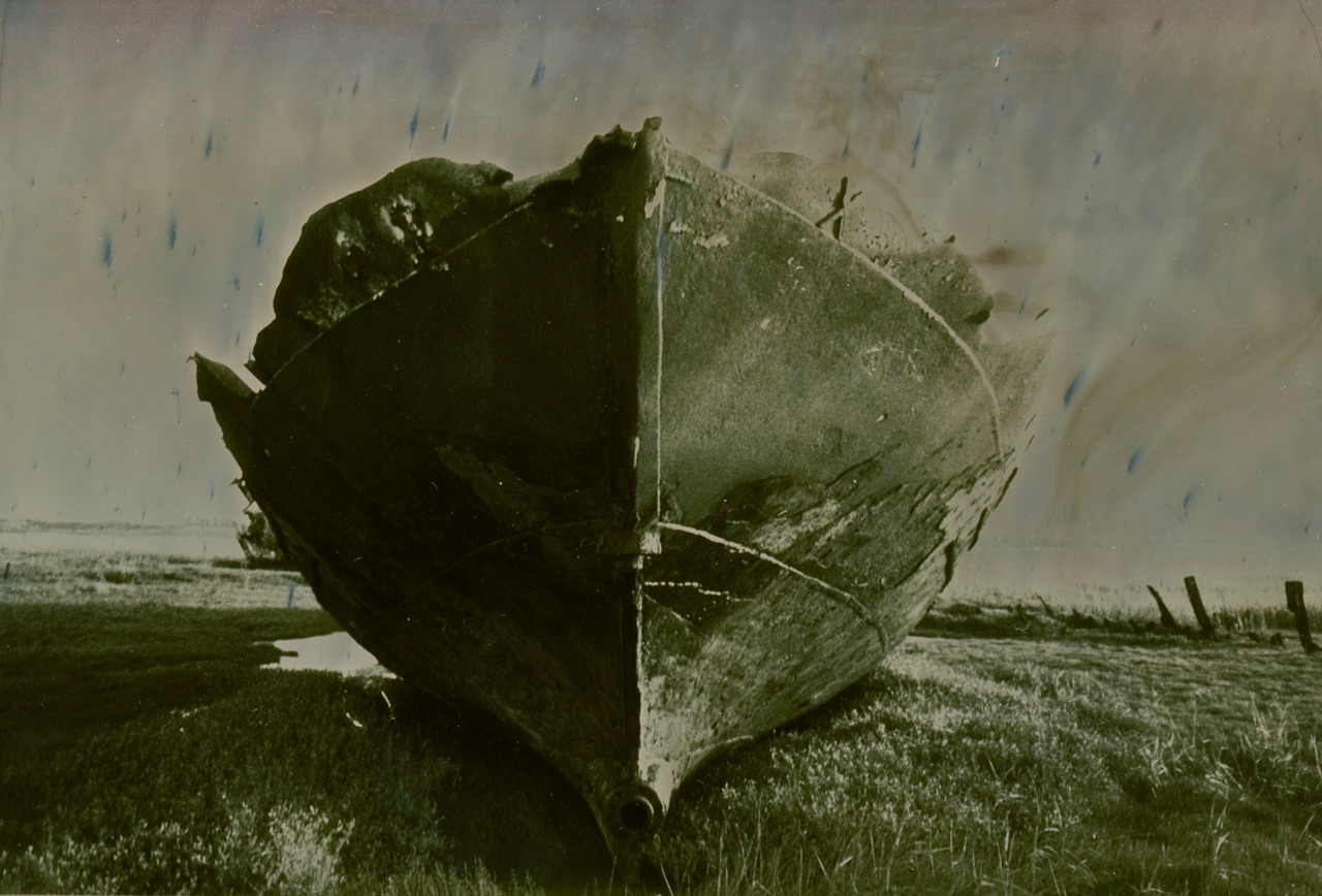 A beached boat hull against a cool grey sky, silver mirror toned on Ilford Pearl RC